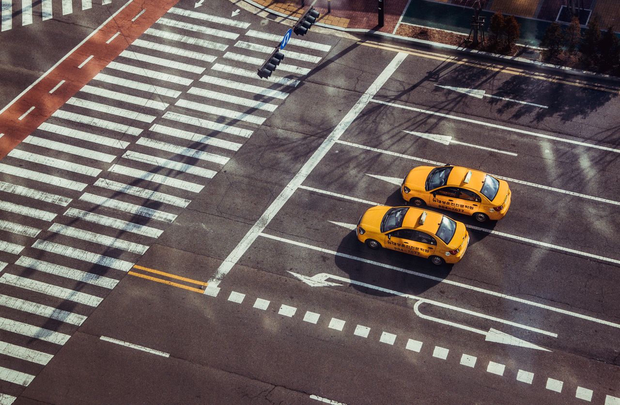 Home Two yellow taxis navigate a city intersection with marked pedestrian crossings.